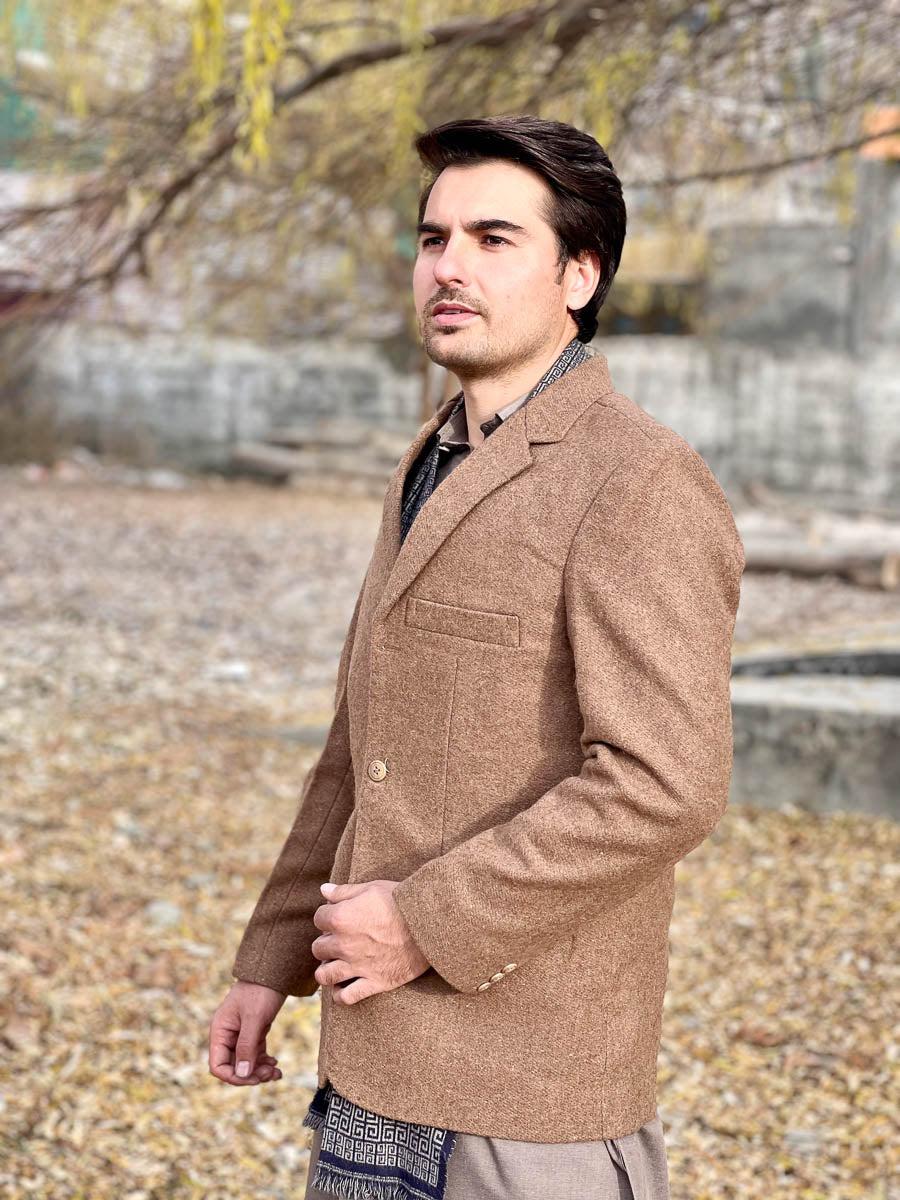 Man wearing a brown coat standing outdoors with trees and ground visible