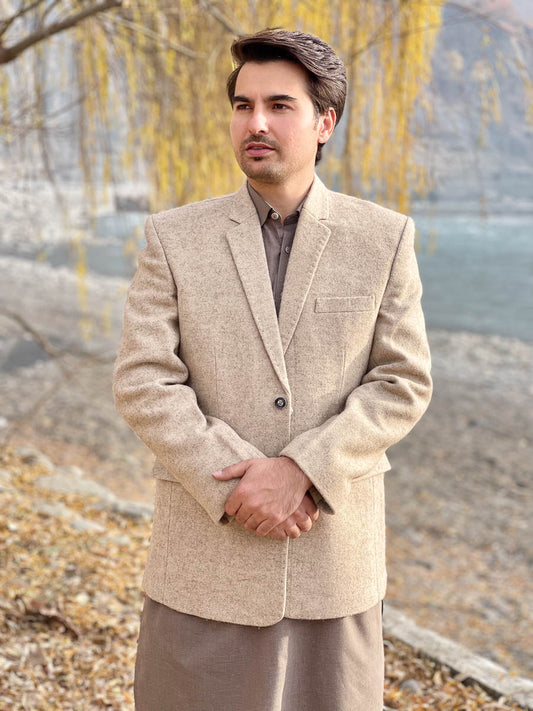 Man wearing a Cream color woolen blazer and light brown pants standing outdoors with trees in the background.