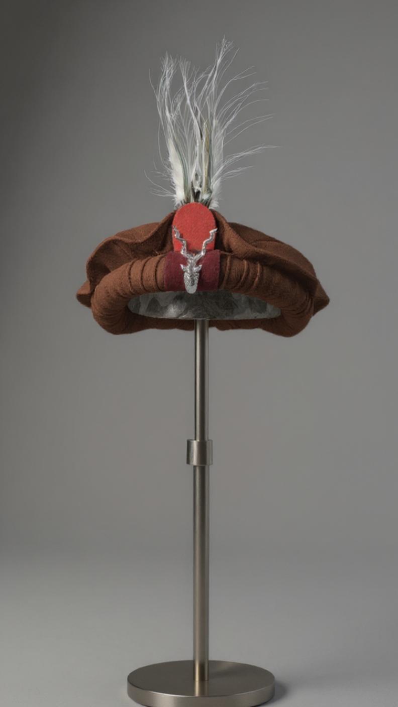 Brown Chitrali Cap with red center and white feather on a gray background